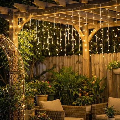 Solar-powered LED icicle string lights from Garden Sanctuary with remote control, hanging outdoors with warm glowing bulbs.